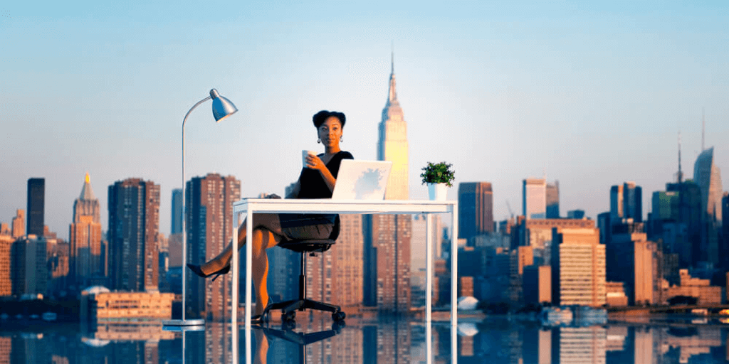 African-American woman sitting at her desk working in NYC with the city skyline in the background